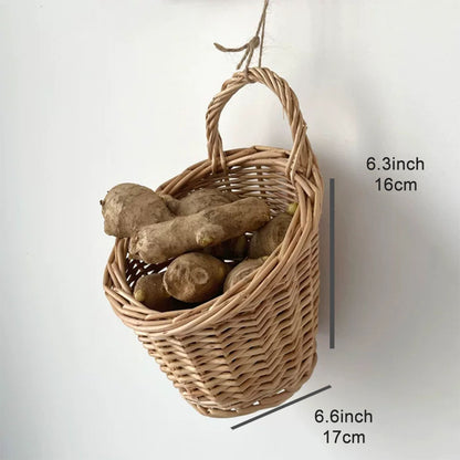 A woven hanging basket made of natural light brown wicker, shown with a hanging loop and filled with root vegetables. 