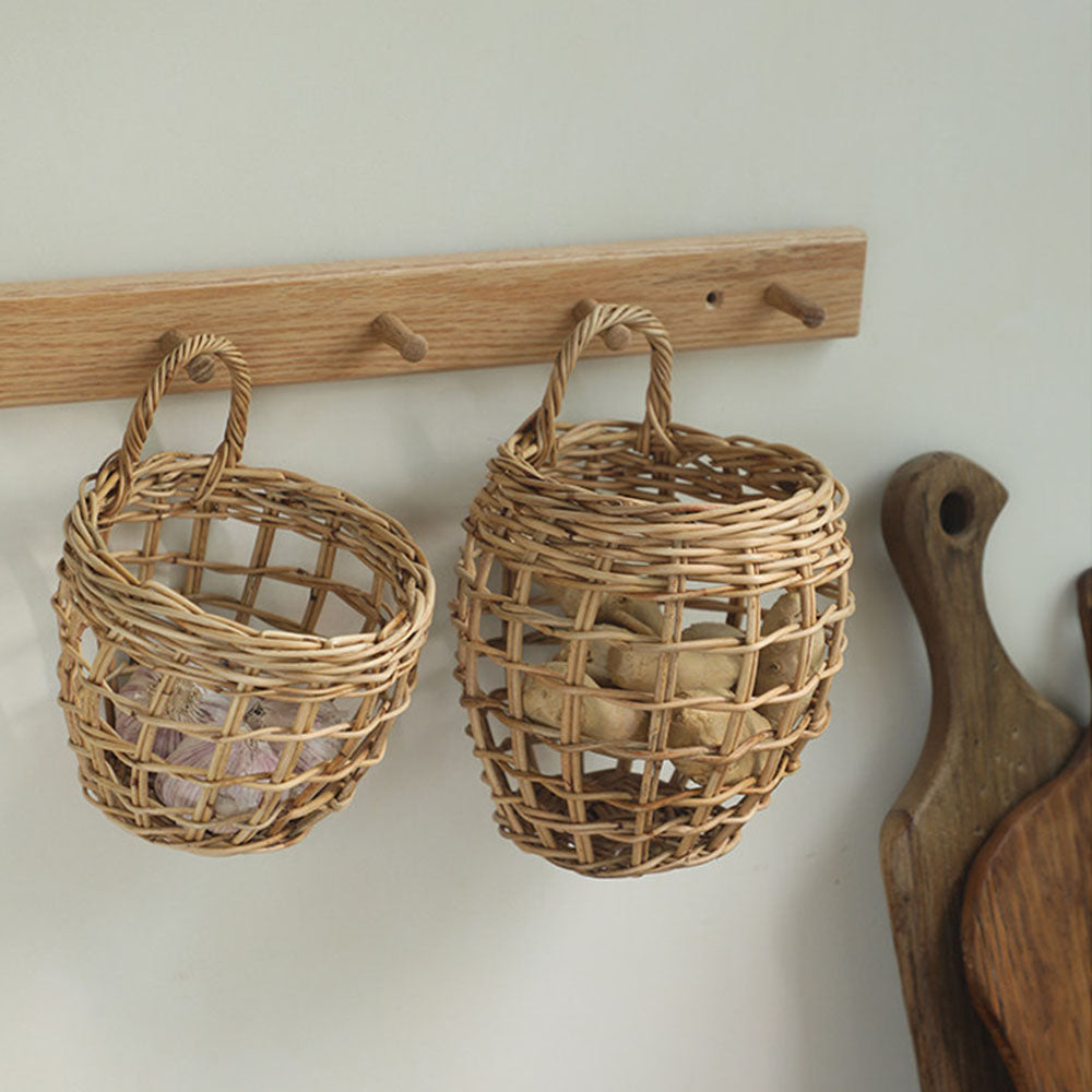 Two woven wicker baskets hanging from a wooden peg rack on a light wall, with neutral decorative items inside.