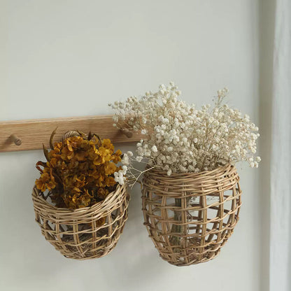 Two woven rattan wall baskets hanging on a light wood rail against a white wall, one holding dried yellow-orange flowers and the other holding dried white baby's breath.
