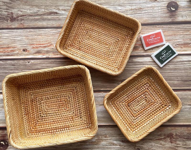 Set of three rectangular rattan baskets in various sizes, with the smallest containing a white coffee mug molded with the word 'coffee', placed on a wooden surface.